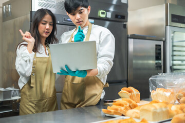 Young asian male and African female in apron using laptop and talking to clients on the phone by workplace.Couple  seller browsing online on cellphone. Bakery shop Business  concept. Retail industry.