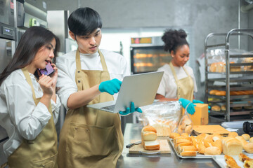 Young asian male and African female in apron using laptop and talking to clients on the phone by workplace.Couple  seller browsing online on cellphone. Bakery shop Business  concept. Retail industry.