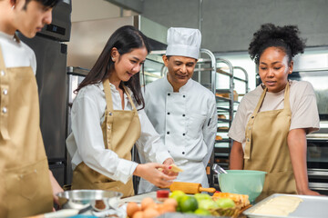 Students In Cookery Class Mixing Ingredients For Recipe In Kitchen.Male And Female young  Students With chef Teacher Preparing Ingredients For Dish In Kitchen Cookery Class.