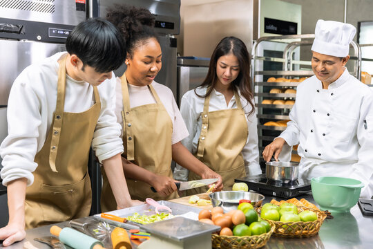 Cooking course , senior Asian male chef in cook uniform teaches young asian and african american people cooking class students to prepare, mix ingredients for pastry foods, fruit pies in restaurant . - Powered by Adobe
