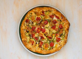 Open shortbread pie with zucchini, tomatoes, sweet peppers and mozzarella cheese on a ceramic plate on a light concrete background. Italian food.