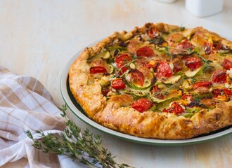 Open shortbread pie with zucchini, tomatoes, sweet peppers and mozzarella cheese on a ceramic plate on a light concrete background. Italian food.