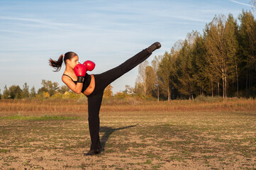 Young woman kickboxing and exercising in the nature on a sunny summer day 