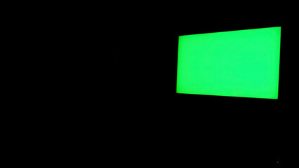 Green screen isolated on black background. Concept. TV with glowing chroma key hanging on the black...