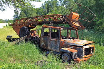 A charred truck on the side of the road in the green grass. A blown up and burnt car at war. Civilian casualties and victims. Technical machine (vehicle) of electricians, blown up by a shell or bomb