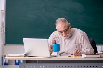 Old male teacher drinking coffee in the classroom