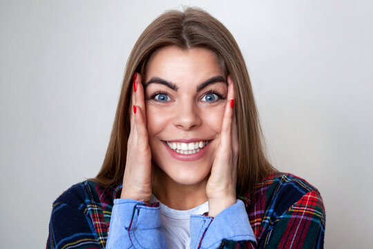 Studio portrait of happy surprised young woman in plaid shirt posing against wall.