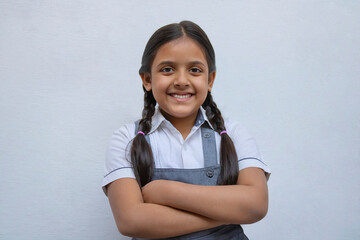 Happy Indian school girl standing against white wall