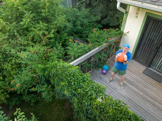 senior man is exercising with a heavy slam ball on his backyard patio, summer aerial view
