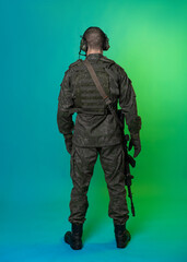 soldier in the studio on a green background with colored light. a man in military uniform with a gun, rifle or machine gun. military. airball player