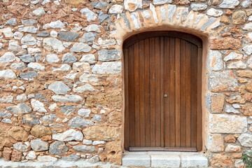 Fototapeta na wymiar Traditional rural home facade background. Stonewall cottage exterior with wooden brown door. Greece