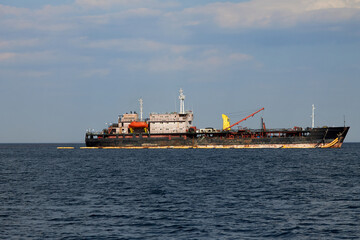 Fototapeta premium Huge military ship sails on a blue sea in clear weather. Modern communication equipment and a crane are installed on the ship.