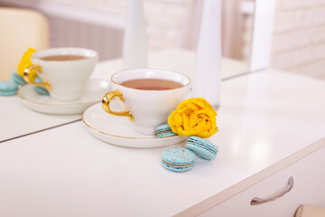 Cup of tea, sweet macaroons and yellow rose on white table
