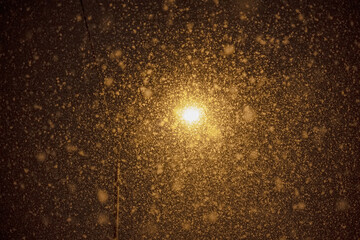 street lamp burning in the dark during a snowstorm, illuminating the falling snow flakes
