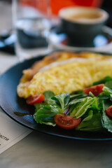 Breakfast in restaurant: yummy omelet with cheese and vegetables, chopped tomato and spinach