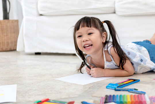 A 3 year old Asian baby girl Lying on the floor,  are concentrating make art by using colored pencils, concept to children and education online.