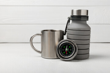 Set of tourist equipment on white wooden background.EDC set.Camping bottle, mug and compass.Copy space.Travel concept.Set of tourist equipment