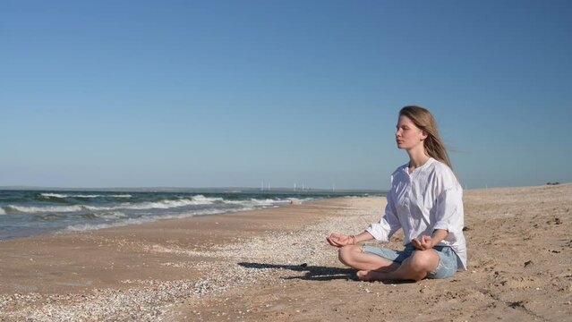 Girl meditating by the sea. Wind shakes long blond hair