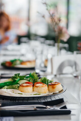 Exquisite breakfast in a luxury restaurant. Cheesecakes with sour cream and greens - lettuce and tomato slices. Served table: fork, knife, napkins, plate