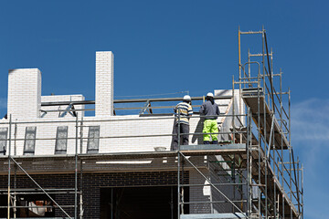 Naklejka premium Dos obreros trabajando en la construcción de una casa subidos en un andamio.