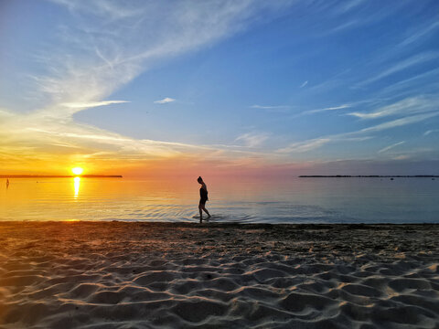 Eine Frau läuft allein im Wasser an der Ostsee bei Sonnenuntergang