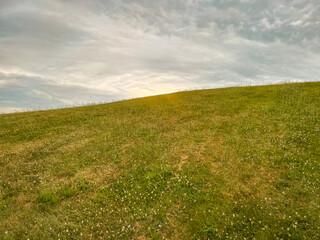 Idyllic Green Hill and Meadow Outdoor Summer Scene. Low-angle view of a fresh vivid green outdoor scene. Lush meadow of grass in the foreground. A large green hill stands tall in the background.