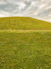 Idyllic Green Hill and Meadow Outdoor Summer Scene. Low-angle view of a fresh vivid green outdoor scene. Lush meadow of grass in the foreground. A large green hill stands tall in the background.