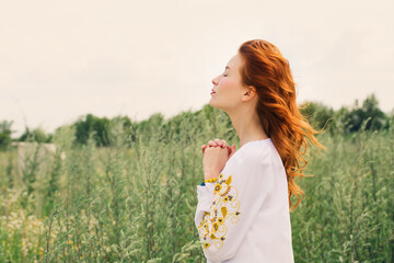 woman in a Ukrainian embroidered shirt prays for Ukraine in the field