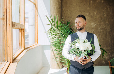 Stylish groom with a bouquet in his hands, looking out the window