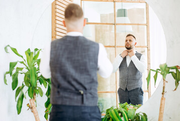 The groom looks at himself in the mirror, fixing his tie.