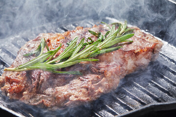 the cook prepares a meat steak on a grill pan close-up, on a dark background