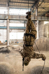 A soldier in camouflage trains fast military rappels upside down with a gun upside down with a gun....