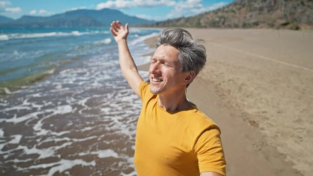 close up selfie portrait of happy middle aged greyhead man at sea coast enjoys sunny day on beautiful sandy beach Iztuzu in Turkey. inspired enjoyed man makes video call and talks about his place
