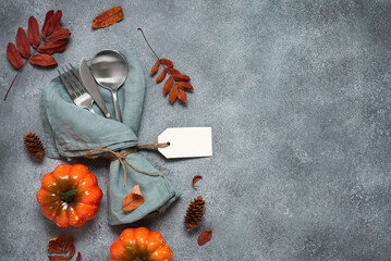 Thanksgiving autumn place setting with cutlery, decorative pumpkins and colorful leaves. Top view,...
