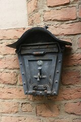 An old metal mailbox with an unusual shape hanging on a brick wall.