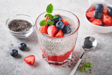 Chia strawberry pudding. Healthy vegan breakfast chia seeds pudding with fresh berries and mint in glass on gray concrete background. Concept of healthy eating, dieting, fitness menu. Selective focus.