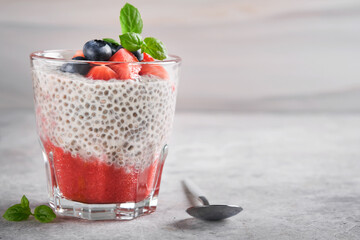 Chia strawberry pudding. Healthy vegan breakfast chia seeds pudding with fresh berries and mint in glass on gray concrete background. Concept of healthy eating, dieting, fitness menu. Selective focus.