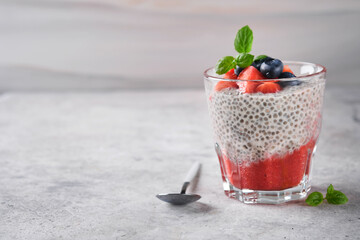 Fototapeta na wymiar Chia strawberry pudding. Healthy vegan breakfast chia seeds pudding with fresh berries and mint in glass on gray concrete background. Concept of healthy eating, dieting, fitness menu. Selective focus.