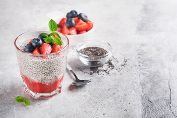 Chia strawberry pudding. Healthy vegan breakfast chia seeds pudding with fresh berries and mint in glass on gray concrete background. Concept of healthy eating, dieting, fitness menu. Selective focus.