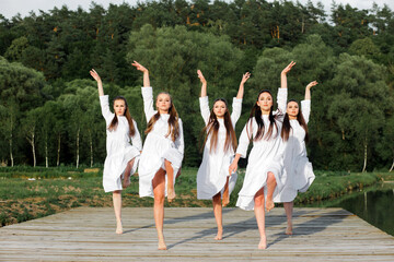 Ukrainian young girls in white dresses dance a stage dance in traditional style on a wooden pier...