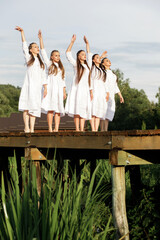 Ukrainian young girls in white dresses dance a stage dance in traditional style on a wooden pier against the background of nature and landscapes.