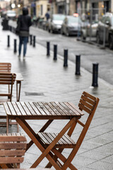 An empty outdoor area of a traditional french restaurant or cafe in a historic downtown. Tables and chairs without visitors.  Business in HoReCa. A rain droplets on table.