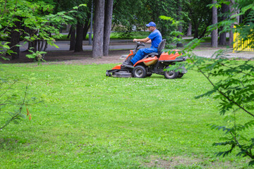 Red Ride-On Lawn Mower on green lawn with driving man outdoors in park. Using technology