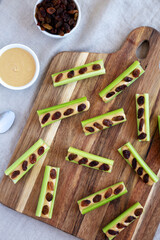 Homemade ants on a log with celery, peanut butter and raisins on a wooden board, top view. Flat lay, overhead, from above.