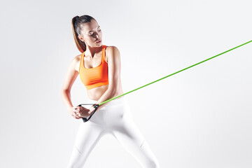 Concentrated woman using resistance band while exercising against white background