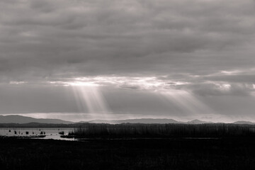 Sunrays at near sunset, with dark clouds in the background, above Trasimeno lake, Umbria, Italy