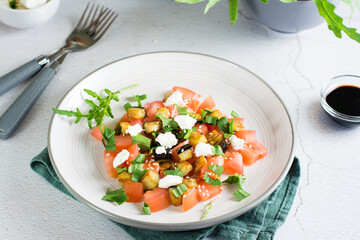 Salad of fried eggplant, tomato, ricotta and arugula on a plate on the table. Homemade lunch