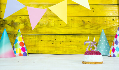 Colorful card happy birthday with festive decorations with cake and burning candles. Copy space. Beautiful happy birthday background on the background of yellow boards with a number  75