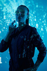 Confident young woman in futuristic glasses standing against colorful background