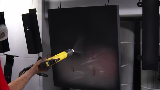 Powder coating of metal products. Employee in a protective mask with an aerosol pistol Kraskit metal parts with black color
